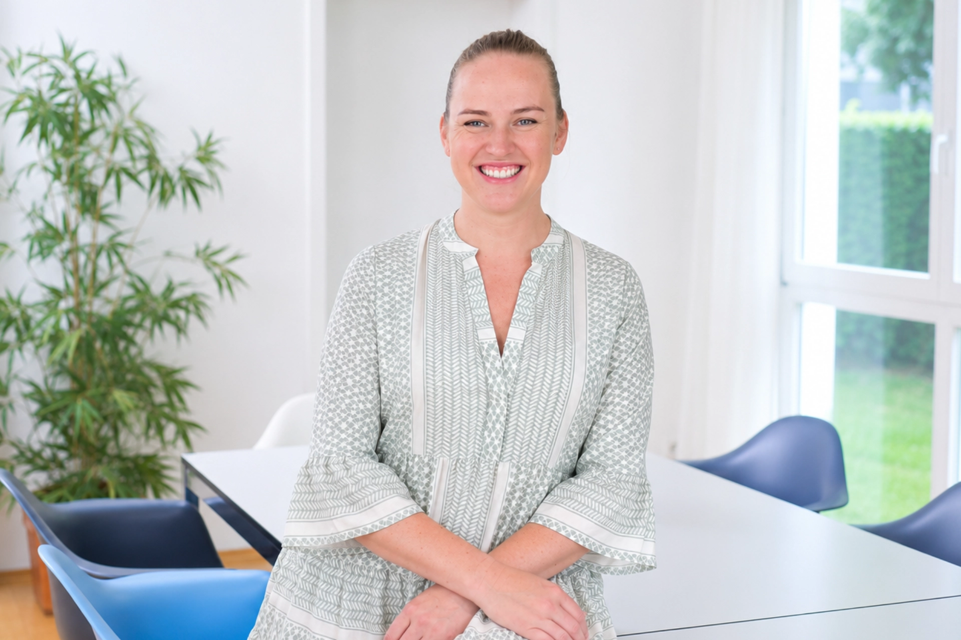Marleen Sicker lächelt in einem hellen Besprechungsraum bei Immobilien Schulte, vor weißen Wänden, großen Fenstern und blauen Stühlen.